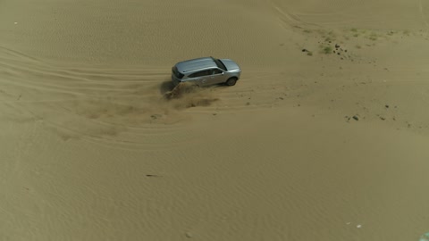 Recreational activities for driving cars in desert areas, a safari adventure on the sand dunes in the Kingdom of Saudi Arabia, drone photography of an Isuzu off-road vehicle on the golden desert sands, sand hills, and rock formations in the Arab deserts.