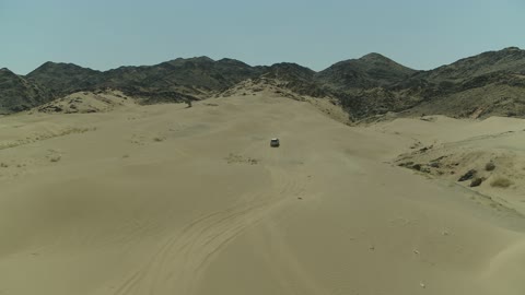 The sand dunes and rock formations in the Arab deserts, recreational activities for driving cars in desert areas, a safari adventure on the sand dunes in the Kingdom of Saudi Arabia, drone photography of an Isuzu off-road vehicle on the golden desert sands.