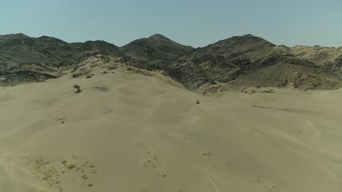 Recreational activities for driving cars in desert areas, a safari adventure on the sand dunes in the Kingdom of Saudi Arabia, drone photography of an Isuzu off-road vehicle on the golden desert sands, sand hills, and rock formations in the Arab deserts.