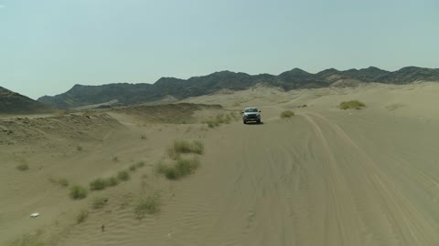 Recreational activities for driving cars in desert areas, a safari adventure on the sand dunes in the Kingdom of Saudi Arabia, drone photography of an Isuzu off-road vehicle on the golden desert sands, sand hills, and rock formations in the Arab deserts.
