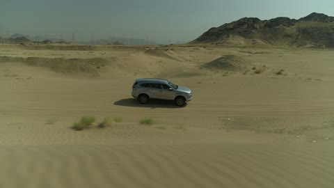 Safari adventure on the sand dunes in the Kingdom of Saudi Arabia, drone footage of an Isuzu off-road vehicle on the golden desert sands, the sand hills and rock formations in the Arab deserts, recreational activities for driving in desert areas.