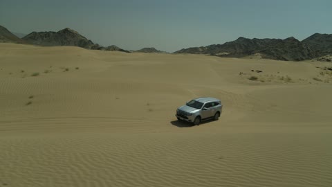 Safari adventure on the sand dunes in the Kingdom of Saudi Arabia, drone footage of an Isuzu off-road vehicle on the golden desert sands, the sand hills and rock formations in the Arab deserts, recreational activities for driving in desert areas.