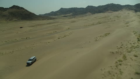 Recreational activities for driving cars in desert areas, a safari adventure on the sand dunes in the Kingdom of Saudi Arabia, drone photography of an Isuzu off-road vehicle on the golden desert sands, sand hills, and rock formations in the Arab deserts.