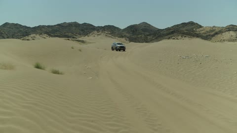 Safari adventure on the sand dunes in the Kingdom of Saudi Arabia, drone footage of an Isuzu off-road vehicle on the golden desert sands, the sand hills and rock formations in the Arab deserts, recreational activities for driving in desert areas.