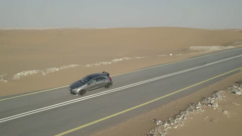 The sand hills and rock formations in the Arab deserts, recreational activities for driving cars in desert areas, the sand dunes in the Kingdom of Saudi Arabia, drone footage of a Mercedes on an asphalt road between the desert and the golden sand dunes.