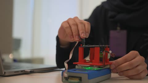 روبوت و نموذج أولي إلكتروني مصغر لشيء ما، موظفة عربية خليجية سعودية تقوم بالعمل عبر اللابتوب المحمول في شركة، جلسة برمجة و اختبار و تصميم بمساعدة الكمبيوتر، مهن ووظائف في شركات المملكة العربية السعودية