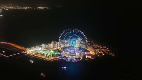 The towers, skyscrapers, and waterfront structures, drone footage of the Dubai Eye in the United Arab Emirates at night, the seaside destination on the Arabian Gulf coast, the architectural engineering art of famous areas and recreational landmarks.