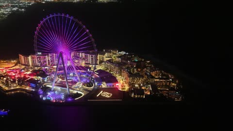 The towers, skyscrapers, and waterfront structures, drone footage of the Dubai Eye in the United Arab Emirates at night, the seaside destination on the Arabian Gulf coast, the architectural engineering art of famous areas and recreational landmarks.