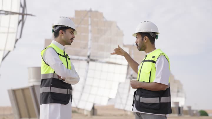 الرقابة على المشروع الهندسي, تبادل الخبرة و الرأى,  مهندسان عربيان خليجيان سعوديان يشرفان على محطات الطاقة الشمسية ينظران الى شىء ما ، إرتداء خوذة وسترة الحماية ، الإشراف على العمل، أنظمة الطاقة الشمسية