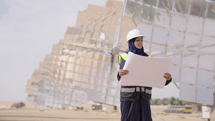 مفهوم ادارة المشروع الهندسي, مهندسة عربية خليجية سعودية محجبة مبتسمة ترتدي العباءة السوداء و الخوذة وسترة الحماية تحمل مخطط و تصميم هندسى, مهن ووظائف سعودية، محطات الطاقة الشمسي