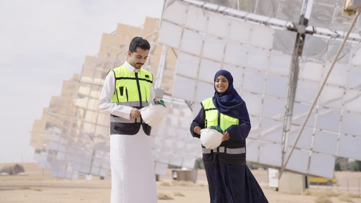 الوقوف بأيدى متقاطعة, إرتداء خوذة وسترة الحماية, مهندسة عربية خليجية سعودية محجبة مبتسمة ترتدي العباءة السوداء تقف بجانب مهندس عربى خليجى سعودى ينظران الى الكاميرا بتعابير السرور و الثقة, مهن ووظائف سعودية