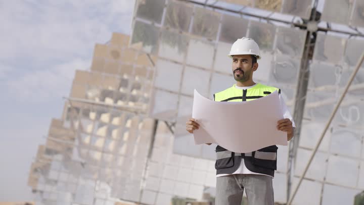 الاشراف على تطبيق المشروع والخطة الهندسيه المعمارية, مهندس عربى خليجى سعودى يرتدى الخوذة وسترة الحماية يمسك مخطط هندسى, التدقيق والإشراف على العمل, مهن ووظائف سعودية، محطات الطاقة الشمسية