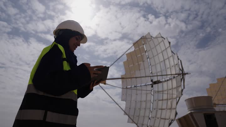 تصوير مقرب لمهندسة عربية خليجية سعودية ترتدي الخوذة وسترة الحماية، التدقيق والإشراف على العمل، مفهوم هندسة الطاقة، مهن ووظائف سعودية، محطات الطاقة الشمسية