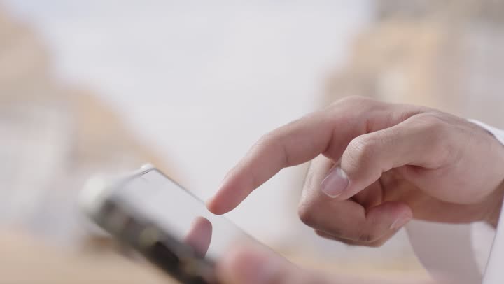 Using a modern technical device, a close-up shot of the hand of a Saudi Arabian Gulf man holding a mobile phone, managing and completing tasks online, communicating with family and relatives.