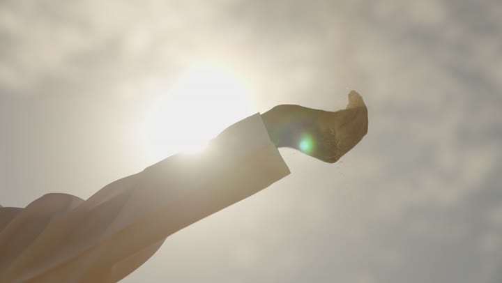 Enjoying the serene natural view in the Kingdom of Saudi Arabia, the sunset over the landscapes and sand dunes in the tourist spots of the Arabian Gulf, the concept of isolation and solitude, a depiction of the hand of an Arab Gulf man in the desert holding soft golden sands in his hands.