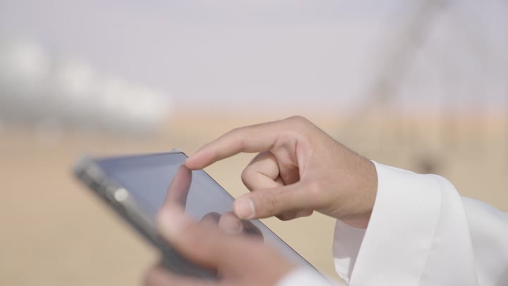 العمل في القطاع الهندسي السعودي، تصوير مقرب ليد مهندس عربي خليجي سعودي يرتدي الثوب التقليدي والسترة وخوذة الحماية يعمل على جهاز التابلت فى الموقع, استخدام جهاز تقني حديث متطور في مجال الهندسة، مفهوم ادارة اشاريع الهندسية والانشاءات