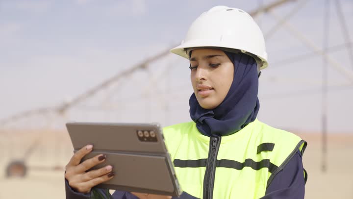 استخدام جهاز تقنى حديث, مهندسة عربية خليجية سعودية مبتسمة ترتدي الحجاب والخوذة وسترة الحماية تمسك بيدها الجهاز اللوحي, تدوين و تسجيل الملاحظات، التأكد من سير الأعمال بالشكل المطلوب والصحيح، كتابة آخر المستجدات حول المشروع