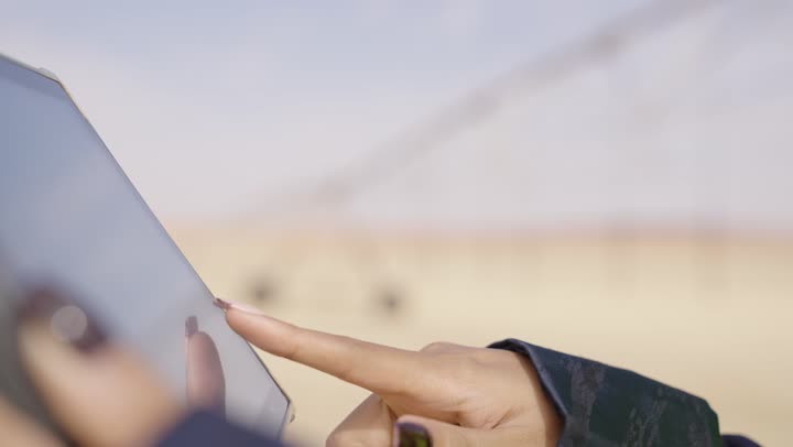 Clicking on the tablet, a close-up shot of the hand of an Arab Gulf Saudi female engineer wearing a black abaya and a safety vest using the tablet, professions and jobs for women.