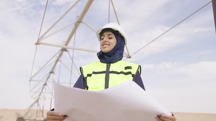 تطوير و بناء المملكة العربية السعودية على يد النساء,  تصوير مقرب لمهندسة عربية خليجية سعودية محجبة ترتدي خوذة الحماية و السترة تحمل بيدها مخطط البناء، الإشراف على المشاريع الهندسية في موقع العمل
