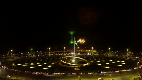 Enjoying fireworks during holidays and occasions, celebrations and festivals in the Kingdom of Saudi Arabia, colorful fireworks in the night sky, participating in recreational activities and festive events, the flag of the Kingdom of Saudi Arabia waving, with the backdrop of the Khobar Tower.