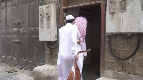 Embodiment of the meanings of nobility and humanity, visual impairment, a portrait of a young Arab Gulf Saudi man wearing a white thobe and a cap helping a blind man to assist him in moving to the right place.