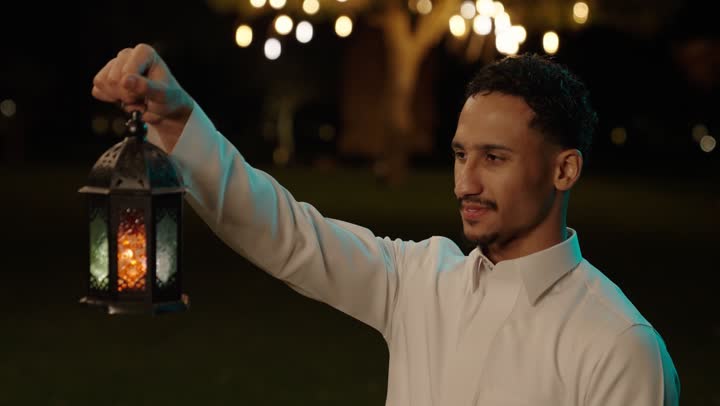 فرحة استقبال شهر رمضان، الأجواء الرمضانية الليلية، تصوير مقرب لرجل عربي خليجي سعودي يرتدي الثوب الابيض يمسك بيدية فانوس معدني مزخرف ، ايماءات السعادة و السرور