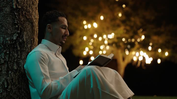 الاستمتاع باوقات الفراغ ، ثقافة التعلم الذاتي، قراءة الكتب بتمعن ، رجل عربي خليجي سعودي يرتدي الثوب التقليدي  يجلس فى الهواء الطلق يحمل بيده كتاب تثقيفي ، إيماءات التركيز والاندماج ، قراءة الروايات والقصص