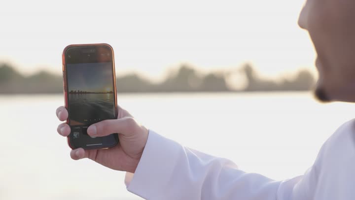 توثيق اللحظات السعيدة، مفهوم الاستجمام والاختلاء, الاسترخاء في الهواء الطلق, تصوير مقرب لرجل عربي خليج سعودي يرتدي الثوب الابيض يقوم بالتقاط صور سيلفي للتذكارعبر الهاتف المحمول , القيام بالأنشطة الممتعة في الإجازة