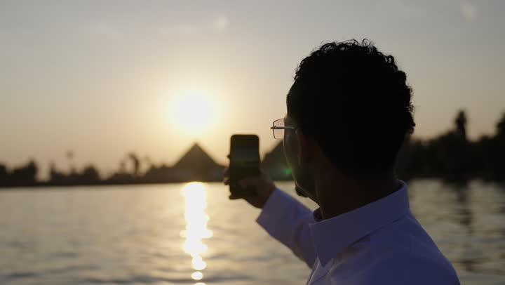 مفهوم الاستجمام والاختلاء, الاسترخاء في الهواء الطلق,تصوير مقرب لرجل عربي خليجي سعودي يرتدي الثوب الابيض يقوم بالتقاط صور سيلفي للتذكارعيبر الهاتف المحمول, القيام بالأنشطة الممتعة في الإجازة