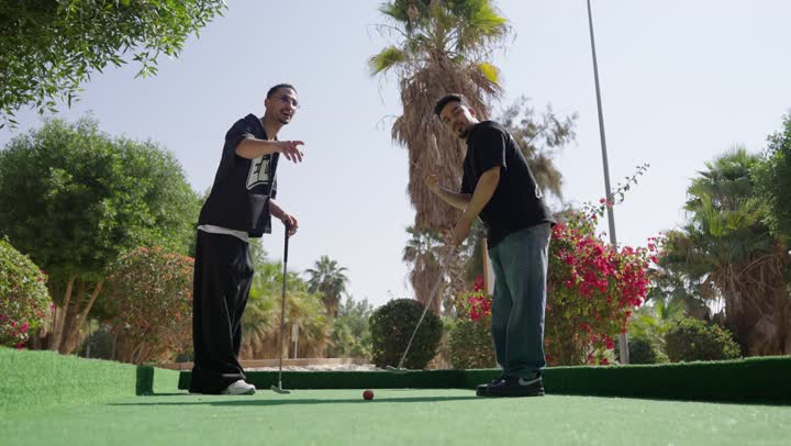 الاشارة الى شيء ما، شابان عربيان خليجيان سعوديان يرتديان الزي الرياضي يقومان بالمصافحة و يمسكان مضرب الجولف، ممارسة لعبة الغولف على مساحات واسعة خضراء، الاستعداد للعب والتنافس، رياضات الألعاب الأولمبية الصيفية، أنشطة ترفيهية مسلية