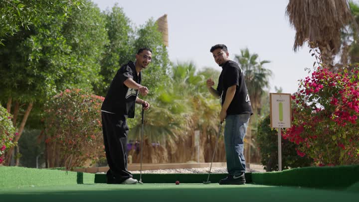 ايماءات السعادة و السرور، شابان عربيان خليجيان سعوديان يرتديان الزي الرياضي يقومان بالمصافحة و يمسكان مضرب الجولف، ممارسة لعبة الغولف على مساحات واسعة خضراء، الاستعداد للعب والتنافس، رياضات الألعاب الأولمبية الصيفية، أنشطة ترفيهية مسلية