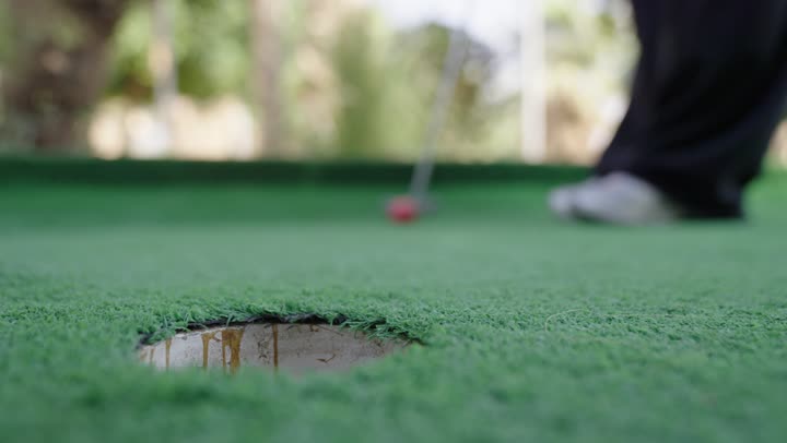 أنشطة رياضية بالسعودية، تحديد وتصويب الهدف، تصوير مقرب لرجل عربي خليجي سعودي يرتدي الزي الكاجوال يقوم بشوط كره الغولف على مساحات واسعة خضراء