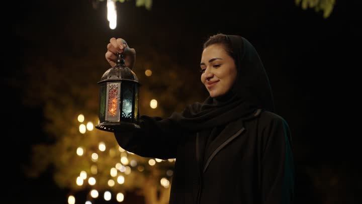 الاحتفال بالمناسبات الدينية الإسلامية، تعابير السعادة و السرور، البهجة بقدوم شهر الخير، التحضير لاستقبال رمضان المبارك,   امراة عربية خليجية سعودية محجبة ترتدي العباءة تمسك بيدها فانوس معدني مزخرف