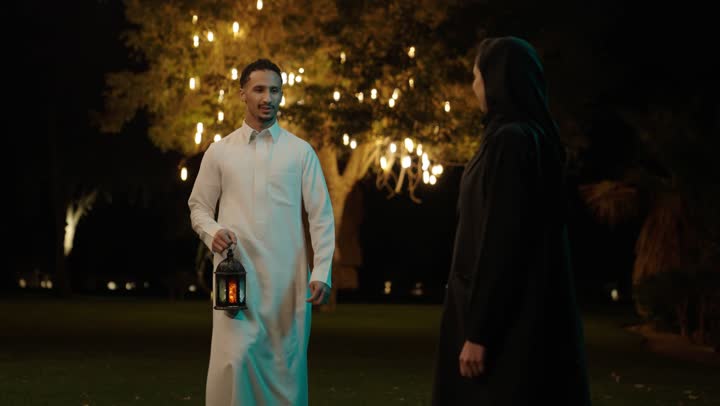 Decorations and ornaments for celebrations in the Kingdom, the religious occasion and Islamic holiday, welcoming the month of goodness and blessings, preparing for the arrival of the month of Ramadan. An Arab Gulf Saudi man wearing a white thobe is giving his wife a metal lantern, expressions of happiness and joy.