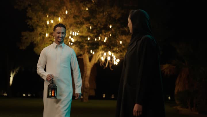 The religious occasion and Islamic holiday, welcoming the month of goodness and blessings, preparing for the arrival of the month of Ramadan, an Arab Gulf Saudi man wearing a white thobe giving his wife a metal lantern, decorations and ornaments of celebrations in the kingdom, expressions of happiness and joy.