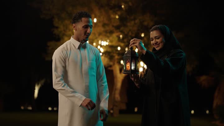 Preparation for the arrival of the month of Ramadan, welcoming the month of goodness and blessings, the religious occasion and Islamic holiday, a Saudi Arabian Gulf man wearing a white thobe giving his wife a metal lantern, decorations and ornaments for celebrations in the kingdom, expressions of happiness and joy.