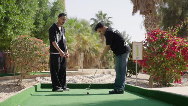 شابان عربيان خليجيان سعوديان يرتديان الزي الكاجوال يقومان بممارسة لعبة الغولف على مساحات واسعة خضراء، أنشطة رياضية بالسعودية،رياضات الألعاب الأولمبية الصيفية، أنشطة ترفيهية