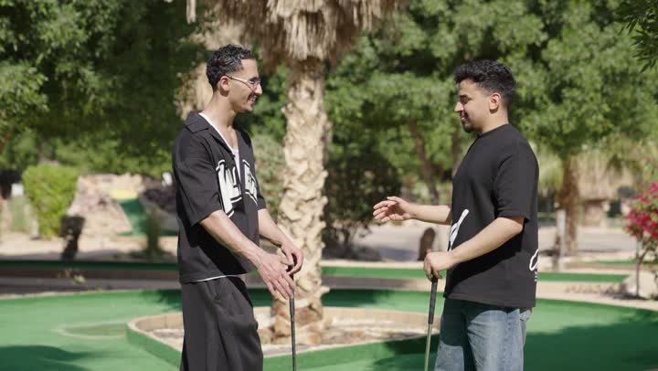 أنشطة ترفيهية مسلية، شابان عربيان خليجيان سعوديان يرتديان الزي الرياضي يقومان بالمصافحة و يمسكان مضرب الجولف، ممارسة لعبة الغولف على مساحات واسعة خضراء، الاستعداد للعب والتنافس، رياضات الألعاب الأولمبية الصيفية