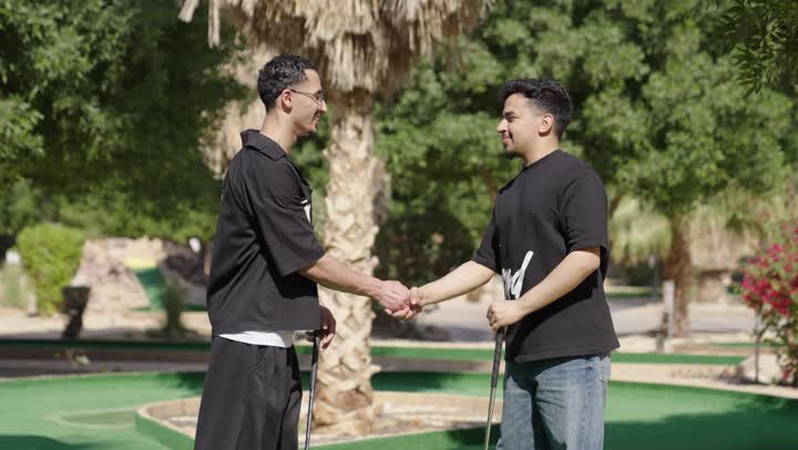 شابان عربيان خليجيان سعوديان يرتديان الزي الرياضي يقومان بالمصافحة  و يمسكان مضرب الجولف، ممارسة لعبة الغولف على مساحات واسعة خضراء، الاستعداد للعب والتنافس، رياضات الألعاب الأولمبية الصيفية، أنشطة ترفيهية مسلية
