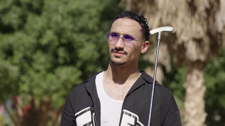 التسلية بالأنشطة البدنية في الهواء الطلق، رجل عربي سعودي خليجي يرتدي الزي الكاجوال يضرب بكفه كره الجولف عدة مرات يمسك المضرب، الاستعداد للعب والتنافس، النظر للكاميرا بايماءات السعادة و السرور
