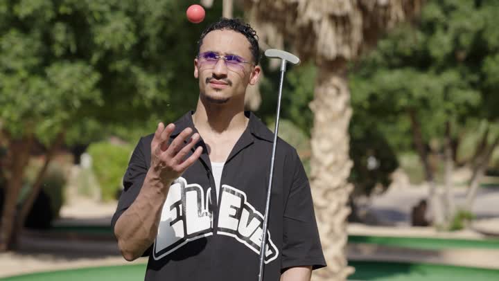 ممارسة الأنشطة الحركية للمتعة في الخارج، رجل عربي سعودي خليجي يرتدي الزي الكاجوال يضرب بكفه كره الجولف عدة مرات يمسك المضرب، الاستعداد للعب والتنافس، النظر للكاميرا بايماءات السعادة و السرور