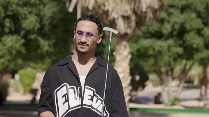 الترفيه وممارسة الألعاب الحركية الخارجية، رجل عربي سعودي خليجي يرتدي الزي الكاجوال يضرب بكفه كره الجولف عدة مرات يمسك المضرب، الاستعداد للعب والتنافس، النظر للكاميرا بايماءات السعادة و السرور