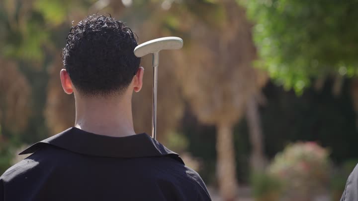 ممارسة الألعاب الحركية للترفيه في الهواء الطلق، قضاء وقت ممتع بالخارج، تصوير من الخلف لزوجان عربيان خليجيان يقومان بالتنزه فى الحدائق يمسكان بيدهم مضرب الجولف، الاستعداد للعب والتنافس