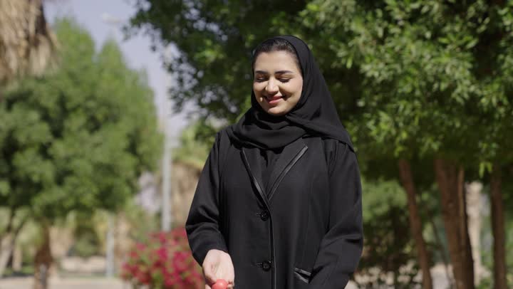 التسليه والترفيه بالالعاب الحركيه في الهواء الطلق، قضاء وقت ممتع بالخارج، امراة عربيه خليجيه سعودية محجبة ترتدي العباءة  تضرب بكرة الجولف عدة مرات و تمسك المضرب، الاستعداد للعب والتنافس