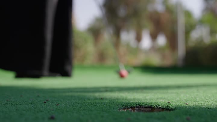 ممارسة لعبة الغولف في مساحات واسعة خضراء، تصوير مقرب لامراة عربيه خليجيه سعودية ترتدي العباءة تمسك المضرب و تقوم بضرب الكرة بعيدا، نشاط رياضي بالمملكة العربية السعودية، الاستمتاع بلعبة الجولف في الملعب، رياضات الألعاب الأولمبية الصيفية