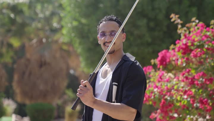 الأنشطة الترفيهية والرياضات الشبابية، ألعاب رياضية ممتعة، شاب عربي خليجي سعودي يرتدي الزي الكاجوال يمسك المضرب ينظر الى الكاميرا بتعابير السعاده والسرور