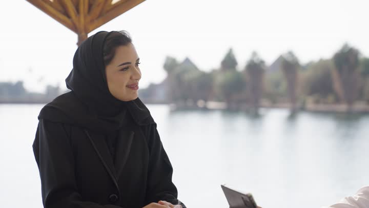 استخدام جهاز تقني حديث، اجواء عائلية سعيدة، مطاعم وكافيهات راقية في السعودية، زوجان عربيان خليجيان سعوديان يرتديان الزي التقليدي  يجلسان فى احد المقاهي الخارجية يقومان بمشاهده شيء ما على جهاز التابلت، نقاشات و حوارات زوجية