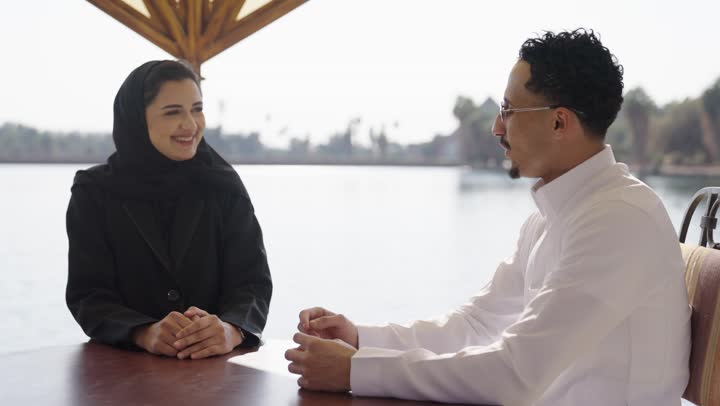 تعزيز الروابط الزوجية والأسرية، جلسة استرخاء في احدي الكافيهات, مفهوم العلاقات الزوجية الناجحة، زوجان عربيان خليجيان سعوديان يجلسان في مقهى خارجي يقومان بالتحدث و المناقشة,  ايماءات السعادة و السرور