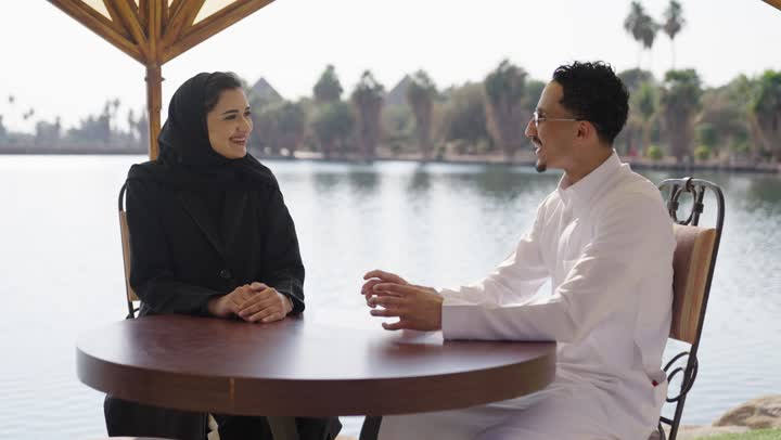 جلسة استرخاء في احدي الكافيهات, مفهوم العلاقات الزوجية الناجحة، تعزيز الروابط الزوجية والأسرية، زوجان عربيان خليجيان سعوديان يجلسان في مقهى خارجي يقومان بالتحدث و المناقشة,  ايماءات السعادة و السرور