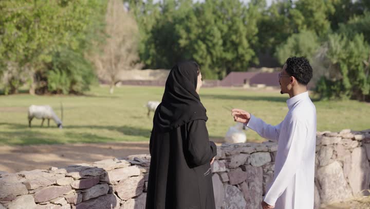 الاشارة الى شيء ما،زوجان عربيان خليجيان سعوديان يرتدي الزي التقليدي يقضيان أوقات ممتعة في إحدى الحدائق في السعودية، اجواء عائلية سعيدة، دردشة ومحادثات زوجية، قضاء عطلة صيفية، نزهه في الهواء الطلق، المشي في الطبيعة الخضراء، أنشطة ترفيهية عائلية